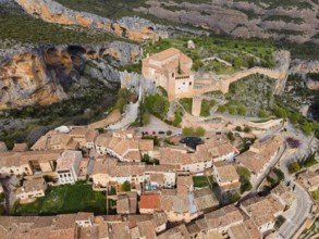 A historic village with tiled roofs and a fortress, nestled in a mountainous landscape, aerial