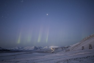 Green northern lights over snow-covered landscape and former cable car, near Longyearbyen,