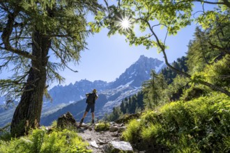 Hiker on hiking trail with sun star, hiking trail La Jonction, behind summit of Aiguille du Midi,