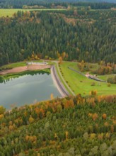 View from above of a lake surrounded by forest and a dam wall in an autumn landscape,