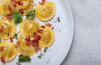 Fresh ravioli, with butter, spices and herbs, fried bacon, on the table, top view, light