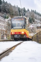 Front view of a tram on snow-covered tracks, surrounded by trees and buildings, Bad Wildbad, Black