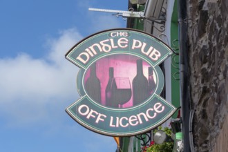 Traditional Dingle pub sign with wine bottles and glass attached to a stone façade under a blue