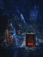 Whisky bottles and a glass of whisky in a blue night scene with water and shadows