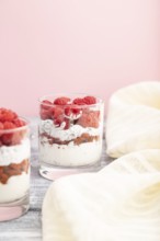 Yogurt with raspberry, goji berries and chia seeds in glass on gray and pink background and linen