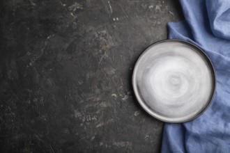 Empty gray ceramic plate on black concrete background and blue linen textile. Top view, copy space,