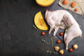 Whole raw rabbit with pumpkin, tomatoes, pea sprouts on a black concrete background and linen