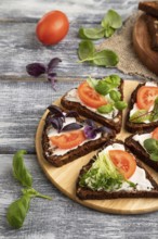 Grain rye bread sandwiches with cream cheese, tomatoes and microgreen on gray wooden background and