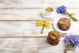 Oatmeal cookies with spring snowdrop flowers bluebells, narcissus and cup of coffee on white wooden