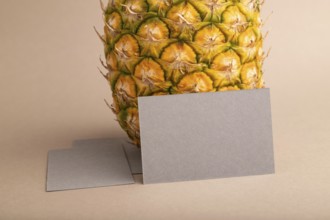 Gray paper business card with ripe pineapple on orange pastel background. Side view, copy space.