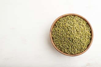 Wooden bowl with raw green mung bean on a white wooden background. Top view, flat lay, copy space