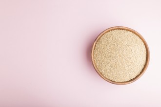 Wooden bowl with raw white quinoa seeds on a pastel pink background. Top view, flat lay, copy space