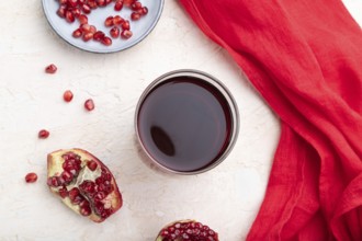 Glass of pomegranate juice on a white concrete background with red textile. Top view, close up,