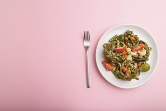 Tagliatelle green spinach pasta with tomato, pea and microgreen sprouts on a pastel pink background