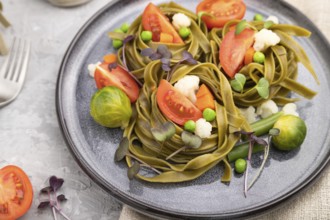 Tagliatelle green spinach pasta with tomato, pea and microgreen sprouts on a gray concrete