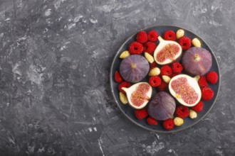 Fresh figs, strawberries and raspberries on blue ceramic plate on black concrete background. top