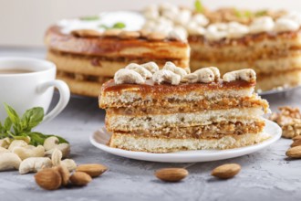 Piece of homemade cake with caramel cream and nuts with cup of coffee on a gray concrete background