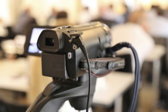 Close-up of a camcorder at a conference or press conference. The guests can be recognised out of