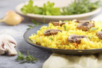 Yellow fried rice with champignons mushrooms, turmeric and oregano on blue ceramic plate on a gray