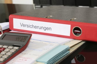 Symbolic image: Folder with insurance policies and calculator on a desk