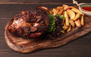 Pork knuckle, in soy-honey sauce, with fried potatoes, on a wooden chopping board, homemade, no