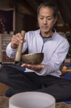 A vertical portrait of a multiracial Latino man with Asian features, holding a Tibetan singing bowl