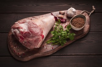 Raw pork knuckle, on a wooden chopping board, with spices, close-up, top view, no people