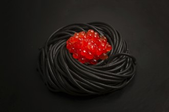 Black spaghetti with red caviar, pasta, on a black background, top view, no people