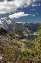 View of the mountain lake Vilsalpsee with surrounding fir trees under a cloudy sky in the