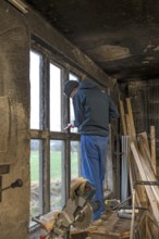 Young man in his workshop, standing on the workbench and repairing a window,