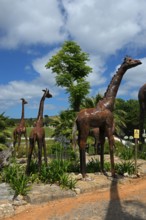 Metal sculptures of giraffes in a natural park setting with trees under a blue sky, Bacalhôa,