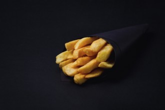 French fries, in black paper packaging, on a black background, close-up, selective focus