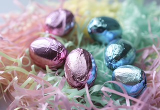 Small chocolate Easter eggs wrapped in shiny foil, placed on a bed of shredded pastel-colored