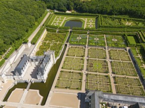 Aerial view of a large castle with symmetrically arranged formal gardens, shaped hedges and water