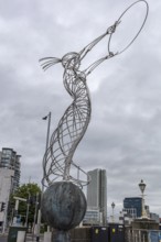 Modern metal sculpture silhouetted against a cloudy sky, surrounded by urban architecture, Belfast