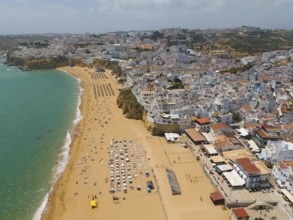 Aerial view of a coastal town with a sandy beach on which numerous parasols and deckchairs can be