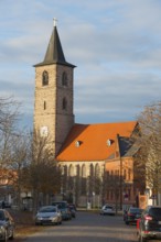 A church with a stone tower and red roof, surrounded by cars and bare trees on a road, St Nikolai