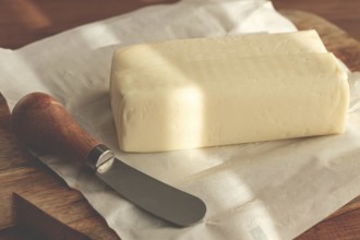 Butter briquette, on wrapping paper, wooden chopping board and butter knife, breakfast, rustic