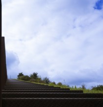 Steep metal stairs, brown, railing at the edge of the picture, green meadow and green bushes on the