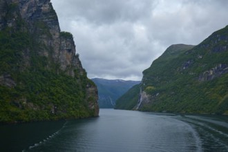 A fjord surrounded by rocky mountains under a cloudy sky with a waterfall in the background,