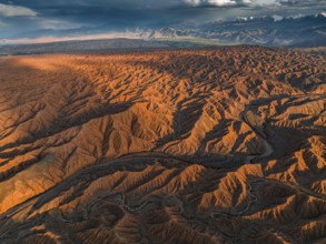 River bed runs through a landscape of eroded hills, badlands at sunset, mountain peaks of the Tian