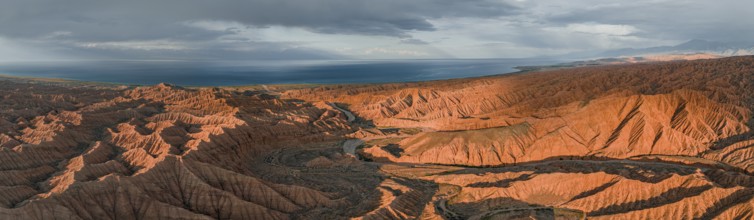 Riverbed runs through a landscape of eroded hills, badlands at sunset, Issyk Kul Lake in the