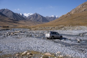 Off-road vehicle crossing a river in the Burkhan valley, mountain landscape with glaciated peaks