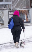 Winter in the city, woman with a small dog on a lead walking through a snowy street, slush,