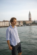 Young man in striped shirt and shorts on the banks of the Grand Canal, behind Campanile, Venice,