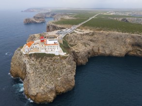 A remote lighthouse and several buildings stand on a cliff, with a wide view of the ocean and the