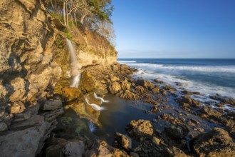 Waterfall falls into the sea on the cliffs, Catarata el Chorro, coastal landscape in the evening