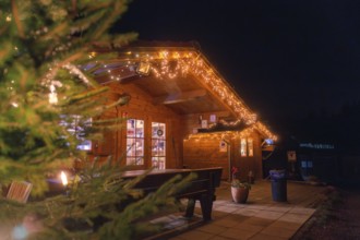 Atmospherically illuminated wooden hut at night with terrace and festive lighting, farm shop,