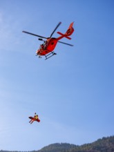 Injured person in a mountain bag with an air rescuer being winched into the rescue helicopter