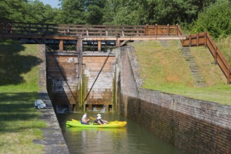 Two yellow kayaks in a canal in front of a closed lock with green and quiet surroundings, Sluza